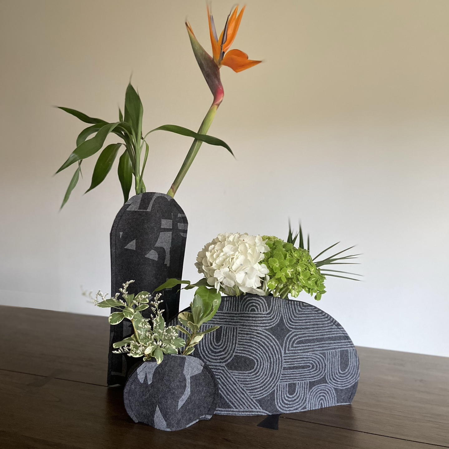 Felt vase sleeve. Handmade, eco-friendly, and sustainable decor. Upcycle recycling through a flexible designed vase cover. This is the triple vase selection of charcoal felt with the Fragment pattern for the tall and round vase sleeve and Rake pattern for the wide.